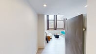 Located on South 47th Street in West Philadelphia, this two-floor, one-bedroom, one-bathroom unit offers a thoughtfully designed layout that maximizes its compact footprint across two distinct levels. The main floor serves as the living and kitchen area, immediately impressing with its dramatic double-height ceilings that amplify the sense of openness. Oversized windows flood the space with natural light while framing views of the surrounding neighborhood. Light wood flooring runs throughout, complementing the bright white walls and creating a clean, modern aesthetic. A compact kitchen with wooden cabinetry and stainless steel appliances is neatly integrated into the main floor.

A sleek metal-railed staircase leads to the upper level, where the spacious bedroom occupies the full floor. Exposed beams and ductwork are painted white, lending the room an industrial-chic character. The generous bedroom offers ample room for sleeping and working areas, with a hallway connecting to storage space.

The bathroom is finished with large-format marble-patterned wall tiles surrounding a soaking tub and shower combination, neutral floor tiles, and a clean, open vanity. Overall, the unit delivers a modern, loft-inspired atmosphere with functional, well-appointed spaces throughout.
