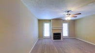 Located at 501 Fairways Dr in Vicksburg, Mississippi, this single-floor home offers a comfortable and functional layout designed for everyday living. The living area serves as the heart of the home, featuring a classic fireplace with a simple mantel that provides a warm focal point for the room. Plush wall-to-wall carpeting runs throughout, adding a soft, comfortable feel underfoot. A ceiling fan with an integrated light fixture is centrally positioned, ensuring year-round comfort and ambient lighting. The room is flanked by multiple windows dressed with white blinds, allowing natural light to filter in while maintaining privacy. A door with a window panel provides direct access to the exterior, enhancing the room's connection to the outdoors. The textured ceiling adds a traditional architectural detail consistent with the home's classic character. An adjacent room features warm-toned walls, offering a distinct and inviting contrast to the main living space. Clean white baseboards frame each room, contributing to a tidy, well-maintained appearance throughout. Overall, this home presents a straightforward, livable floor plan with practical finishes in an established Vicksburg neighborhood.