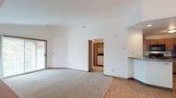 This single-floor residence offers a thoughtfully designed layout with a seamless flow between living, dining, and kitchen spaces. The open-concept living and dining area features a combination of hardwood-style flooring and plush carpeting, with a sliding glass door that invites natural light. A curved breakfast bar separates the kitchen from the living area, providing a practical transition between spaces.

The kitchen is well-equipped with warm oak cabinetry, dark granite-style countertops, and a full suite of black appliances, including an electric range with overhead microwave and a refrigerator. Ample cabinet storage ensures functional organization.

The bedrooms are carpeted and generously sized, with one room showcasing a striking vaulted ceiling that adds architectural interest and a sense of openness. Each bedroom benefits from natural light, with windows offering views of surrounding greenery. Closet space is notably well-planned, including built-in shelving in select areas.

Two bathrooms serve the residence. The primary bathroom features a wide vanity with oak cabinetry, granite-style countertops, and a large mirror with overhead lighting. The secondary bathroom includes a tub and shower combination with a frosted glass sliding door. Both bathrooms are finished with tile flooring.