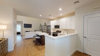 Located at The Villas At Setauket in East Setauket, NY, this two-story villa offers a thoughtfully designed interior defined by clean lines, neutral tones, and quality finishes. The main level centers on an open-concept living area where soaring double-height ceilings amplify the sense of space. A marble-surround fireplace anchors the living room, complemented by warm hardwood flooring that extends throughout the first floor. A dedicated dining nook sits beneath the upper-level balcony railing, adding architectural interest to the space.

The kitchen is well-appointed with white shaker cabinetry extending to the ceiling, quartz countertops featuring subtle veining, and a full suite of stainless steel appliances including a gas range, built-in microwave, refrigerator, and dishwasher. A large peninsula provides additional seating and prep space. A charming half bath on the main level features marble-style tile flooring and an octagonal window.

Upstairs, the primary bedroom is a serene retreat with plush carpeting, a generous window for natural light, and direct access to an en-suite bathroom finished with large-format tile and a sleek frameless glass shower. Additional bedrooms feature hardwood flooring and ample natural light, rounding out a versatile and polished two-story residence.