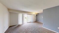 Located at 8569 Greenbelt Rd in Greenbelt, Maryland, this one-bedroom, one-bathroom residence offers a well-organized single-floor layout with a comfortable and functional design throughout. The expansive living room is a central highlight, featuring plush wall-to-wall carpeting, neutral-toned walls with a contrasting slate-blue accent wall, and a pendant light fixture. Sliding glass doors with vertical blinds lead directly to a private balcony, filling the space with natural light and providing outdoor views. The kitchen is equipped with warm oak cabinetry, dark granite-style countertops, a gas range, dishwasher, and black refrigerator, all set atop easy-care hardwood-style flooring. A breakfast bar peninsula adds additional prep and dining space. The generously sized bedroom features carpet flooring, a large window with outdoor views, and access to a spacious walk-in closet outfitted with built-in shelving rods on both sides, offering ample storage. A second closet provides additional storage convenience. The bathroom includes a full tub-shower combination with clean white tile surround and chrome fixtures. Overall, the residence presents a straightforward, practical layout suited for comfortable everyday living.