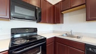 Located at 400 Haslet St in Dover, Delaware, this single-floor residence offers a practical and well-appointed living space. The kitchen is a standout feature, showcasing rich, dark cherry-toned cabinetry that extends from floor to ceiling, providing generous storage throughout. Light countertops offer a clean contrast against the dark cabinetry, creating a classic and timeless aesthetic. The kitchen is fully equipped with black appliances, including an electric range with coil burners, an over-the-range microwave, and a stainless steel sink positioned conveniently along the countertop. The L-shaped kitchen layout maximizes efficiency, allowing for smooth workflow between cooking and prep areas. The white walls and clean lines throughout the kitchen contribute to a bright and tidy atmosphere. The single-floor layout of the home ensures easy accessibility and seamless flow between spaces. Overall, the residence combines functional design with practical finishes, making it a comfortable and well-organized home in the heart of Dover, Delaware.