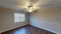 Located in Houston, TX, this single-story 2-bedroom, 1-bathroom home delivers a clean, modern aesthetic with consistent finishes throughout. Dark hardwood-style flooring runs across all living areas, providing a warm contrast against the neutral gray and beige toned walls. Each room features a ceiling fan with integrated lighting, textured ceilings, and white horizontal blinds that allow for natural light while maintaining privacy. A decorative chair rail detail accents several rooms, adding a subtle architectural touch.

The living and dining areas are open and well-proportioned, with the dining space distinguished by an elegant pendant light fixture. The galley-style kitchen is efficiently designed and features white cabinetry with sleek hardware, granite-look countertops, a double stainless steel sink, and a full suite of black appliances including a gas range, microwave, refrigerator, and dishwasher. Track lighting illuminates the workspace effectively.

Both bedrooms are generously sized, each with a ceiling fan and windows that bring in natural light. The full bathroom is neatly appointed with a granite-topped white vanity, a large mirror, tiled tub-and-shower combination, and matching dark flooring, completing a cohesive and updated look throughout the home.