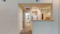 This single-floor residence offers a thoughtfully designed layout that balances comfort and functionality. The living area is generously sized, featuring plush carpeting, a ceiling fan, and large windows with vertical blinds that allow abundant natural light to filter in. A glass door provides direct access to an outdoor space, enhancing the room's connection to the exterior.

The kitchen is efficiently arranged with white cabinetry, a full suite of white appliances including a refrigerator, electric range, built-in microwave, and dishwasher. Tile flooring, a double-basin sink, and a pass-through counter opening to the adjacent living area add to its practicality. A hallway connects the main living spaces to the bedrooms, with HVAC vents and an attic access panel overhead.

The bedrooms are carpeted and well-lit, each equipped with ceiling fans. One bedroom stands out with built-in shelving and a window bench with cabinet storage beneath, offering both display space and additional storage. The primary bathroom features a wide dual-sink vanity with white cabinetry, a warm countertop, and a large mirror with bright Hollywood-style lighting. The layout provides a comfortable, cohesive living environment throughout.