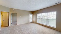 This single-floor space offers a practical and comfortable layout with a clean, neutral aesthetic throughout. The living area is generously sized, featuring plush wall-to-wall carpeting, warm beige walls, and a textured ceiling. Large windows fitted with horizontal blinds flood the room with natural light and provide outdoor views, while a glass-paned exterior door offers convenient access to the outside. An open pass-through connects the living area to the kitchen, enhancing the sense of openness. A chandelier overhead adds a touch of warmth to the dining area nearby.

The galley-style kitchen is efficiently designed, featuring light wood cabinetry, a coil-burner electric range, a built-in dishwasher, a stainless steel sink, and durable tile flooring. Ample counter space and upper and lower cabinet storage make this kitchen highly functional. A utility panel is also accessible from within the kitchen corridor.

The bedrooms continue the carpeted, neutral-toned design, each equipped with windows that bring in natural light and outdoor views. One bedroom includes a mirrored closet door, adding a sense of depth to the space.

The bathroom is well-appointed with a vanity featuring light wood cabinetry, a large mirror, a full tub-shower combination, and tile flooring, completing this thoughtfully arranged and move-in-ready space.