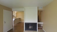 This two-story home offers a functional and well-organized layout across two levels. The main living area is anchored by a striking floor-to-ceiling white-surround fireplace, serving as the focal point of the room and adding a classic, welcoming touch to the space. Rich hardwood flooring extends throughout the main living area, contributing warmth and character to the interior.

Adjacent to the living room, the kitchen is open and accessible, featuring white cabinetry and a countertop bar that creates a natural transition between cooking and living spaces. The kitchen is equipped with appliances including a microwave, and benefits from a ceiling light fixture that ensures a well-lit work environment.

The staircase, positioned to the right of the fireplace, features a white banister and leads to the upper floor, where additional living spaces are found. The neutral, warm-toned walls throughout the home provide a versatile backdrop that complements a variety of furnishing styles.

HVAC vents are visible in the ceiling and walls, indicating a central air system serving both levels. The overall layout is clean and straightforward, making efficient use of the available space while maintaining a cohesive and comfortable atmosphere throughout the home.
