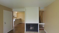 This two-story home offers a functional and well-organized layout across two levels. The main living area is anchored by a striking floor-to-ceiling white-surround fireplace, serving as the focal point of the room and adding a classic, welcoming touch to the space. Rich hardwood flooring extends throughout the main living area, contributing warmth and character to the interior.

Adjacent to the living room, the kitchen is open and accessible, featuring white cabinetry and a countertop bar that creates a natural transition between cooking and living spaces. The kitchen is equipped with appliances including a microwave, and benefits from a ceiling light fixture that ensures a well-lit work environment.

The staircase, positioned to the right of the fireplace, features a white banister and leads to the upper floor, where additional living spaces are found. The neutral, warm-toned walls throughout the home provide a versatile backdrop that complements a variety of furnishing styles.

HVAC vents are visible in the ceiling and walls, indicating a central air system serving both levels. The overall layout is clean and straightforward, making efficient use of the available space while maintaining a cohesive and comfortable atmosphere throughout the home.