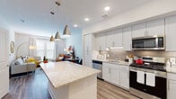 This thoughtfully designed single-floor residence combines modern finishes with a functional, open layout. The kitchen is a standout centerpiece, featuring crisp white shaker cabinetry with brushed nickel hardware, a large granite-topped island illuminated by stylish gold pendant lights, a subway tile backsplash, and a full suite of stainless steel appliances including a gas range, built-in microwave, dishwasher, and refrigerator. Light wood-look flooring flows seamlessly throughout, connecting the kitchen to the open living and dining area. The living space is bright and airy, benefiting from large windows that invite ample natural light, and offers comfortable room for both a seating arrangement and a dedicated dining area. An in-unit stacked washer and dryer provides added convenience. The bedroom is a serene retreat, highlighted by a bold deep-green accent wall, a large window with blinds, and warm, inviting tones that create a cozy atmosphere. The bathroom echoes the home's refined aesthetic with granite countertops, white cabinetry, subway tile surround, and tile flooring. Throughout the space, the consistent use of quality materials and thoughtful design details create a cohesive and contemporary living environment.