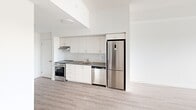 Located at 375 South Street in London, Ontario, this well-appointed 2-bedroom, 1-bathroom unit offers a clean, modern aesthetic throughout its thoughtfully designed single-floor layout. Light-toned hardwood-style flooring runs consistently across the space, complementing the crisp white walls and creating a bright, cohesive atmosphere.

The kitchen is efficiently designed with white flat-front cabinetry extending to the ceiling for maximum storage, a subway tile backsplash, dark countertops, and a full suite of stainless steel appliances including a stove, dishwasher, and tall refrigerator. The open sightlines from the kitchen connect seamlessly to the living area, enhancing the sense of openness.

The primary bedroom is a comfortable retreat featuring a sliding-door closet with built-in hanging storage and neutral white walls. The second bedroom benefits from expansive floor-to-ceiling sliding glass doors with vertical blinds, allowing abundant natural light and offering elevated outdoor views of the surrounding area.

The bathroom is finished with grey tile flooring, a white vanity with a dark countertop, a large mirror, and brushed gold accent hardware, adding a refined touch. The unit's elevated position provides pleasant views visible from both the bedroom and bathroom, enhancing the overall sense of openness and connection to the outdoors.