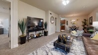 This model unit at 160 Stone Park Blvd in Pike Road, Alabama, offers a thoughtfully designed single-floor layout that balances comfort and functionality. The entry hallway sets a welcoming tone with warm stone-look tile flooring, white panel doors, and decorative wall accents that carry through the home. The galley-style kitchen features rich wood cabinetry, granite countertops, a tile backsplash, and black appliances, providing ample prep and storage space. Adjacent to the kitchen, the dining area is illuminated by a chandelier and offers a warm, inviting atmosphere with earthy tones and eclectic furnishings. The spacious living room is carpeted and bathed in natural light through French doors, creating a relaxed and open atmosphere. The primary bedroom is generously sized with plush carpet, large windows, and a ceiling fan, complemented by a walk-in closet with built-in wire shelving and hanging rods. The bathrooms feature stone-look tile flooring and clean, neutral finishes. A dedicated utility/storage room with multi-tiered wire shelving adds practical value to the home. Throughout, the unit maintains a cohesive palette of warm neutrals, with consistent tile and carpet flooring that connects each space seamlessly.