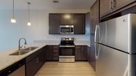 Located at 6315 Portree Harbour Ln in Charlotte, NC, this single-floor residence offers a well-designed layout with modern finishes throughout. The kitchen is a standout feature, showcasing rich dark cabinetry, granite-look countertops, and a full suite of stainless steel appliances including a refrigerator, electric range, and over-the-range microwave. Light wood-tone flooring runs through the kitchen and dining area, enhancing the bright, open feel of the space. Pendant lighting over the kitchen counter adds a stylish touch and seamlessly connects to the adjacent dining area. The living area transitions to plush carpeting, creating a comfortable and inviting atmosphere. A ceiling fan with a built-in light fixture provides both comfort and function. Natural light filters in through windows fitted with white blinds, offering a clean, neutral aesthetic. The primary bathroom includes light wood-tone flooring, dark vanity cabinetry with granite countertops, and direct access to a spacious walk-in closet equipped with multi-tiered shelving and hanging rods. The overall design palette of neutral tones, modern fixtures, and quality finishes gives this residence a clean, contemporary character.