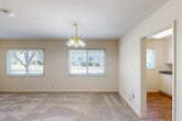Located at 3500 Edison Street in San Mateo, California, this single-floor, 2-bedroom, 1-bathroom home offers a straightforward and functional layout. The living area is bright and welcoming, featuring soft wall-to-wall carpeting, warm neutral-toned walls, and multiple windows that allow abundant natural light to fill the space. A classic brass chandelier serves as a central fixture, adding a touch of traditional charm. Views of surrounding greenery are visible through the sliding and standard windows, enhancing the airy feel of the room.

The kitchen is equipped with white cabinetry, stainless steel countertops, a double-basin sink, and includes essential appliances — a range and a full-size refrigerator. Warm wood-look flooring runs throughout the kitchen, contrasting neatly with the clean white finishes.

The spacious primary bedroom offers generous room dimensions with carpeted flooring and a dedicated closet featuring a built-in shelf and hanging rod for organized storage. The second bedroom is similarly carpeted and well-proportioned.

The bathroom includes a white vanity, a tub/shower combination, and sage green tile wainscoting that adds a retro, classic aesthetic. A frosted window provides natural light while maintaining privacy. Wood-look flooring completes the bathroom's clean, functional design.