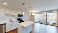 This single-floor residence at 12225 Huffman Rd in Parma Heights, Ohio offers a thoughtfully designed open-concept layout that seamlessly connects the kitchen and living areas. The kitchen is a standout feature, equipped with stainless steel appliances including a range, microwave, dishwasher, and refrigerator, all set against crisp white shaker-style cabinetry and a classic subway tile backsplash. A generously sized center island with a veined quartz countertop serves as a natural focal point, providing additional workspace and casual seating. Pendant lighting above the island and recessed ceiling lights add a modern, layered lighting scheme throughout.

Rich hardwood-style flooring flows continuously from the kitchen into the open living area, which benefits from a large floor-to-ceiling window fitted with vertical blinds, allowing for abundant natural light and views of the surrounding greenery. The living space is open and versatile, offering ample room for a variety of furniture arrangements.

The bathroom features a full tub-shower combination with large-format tile surround and chrome fixtures, maintaining the clean, contemporary aesthetic found throughout the unit. The bedroom is spacious with additional natural light from a dedicated window. Overall, the space presents a fresh, modern interior with neutral tones and quality finishes.