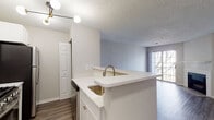 This single-floor residence at 45 Valley Rd in Stamford, Connecticut, offers a thoughtfully designed layout with a clean, contemporary aesthetic throughout. The kitchen serves as a functional centerpiece, featuring white shaker-style cabinetry, light marble-look quartz countertops, and a peninsula with an undermount sink that opens toward the living area. Stainless steel appliances, including a gas range, over-the-range microwave, and refrigerator, complete the well-equipped space. The kitchen flows naturally into the main living area, which is finished with wood-look plank flooring and neutral-toned walls. A tiled fireplace with a white mantel anchors one wall of the living room, while a full-glass sliding door draws in natural light and provides access to an outdoor deck with exterior views. The bedroom is carpeted and features a large window, adding brightness to the comfortable space. The bathroom includes white cabinetry with a clean countertop vanity, a shower-tub combination, and wood-look flooring. Textured ceilings are present throughout the unit, contributing to its residential character. The overall ambiance is bright, neutral, and move-in ready.