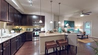 This single-floor residence offers a thoughtfully designed open-concept layout that seamlessly connects the kitchen, dining, and living areas. The kitchen is outfitted with dark espresso cabinetry, stainless steel appliances including a range and built-in microwave, a tile backsplash, and a peninsula island topped with light granite countertops. Three pendant lights hang above the island, which accommodates bar seating with woven stools, creating a casual dining option. Rich hardwood-style flooring grounds the main living area, while recessed and track lighting provide ample illumination throughout.

The bedroom is a serene retreat featuring plush carpeting, a ceiling fan, and a large window dressed with sheer curtains and blinds that invite natural light. The bathroom includes a full soaking tub with a tiled surround, a dark vanity with granite countertops, and large-format tile flooring. A dedicated in-unit laundry room houses a full-size washer and dryer side by side on wood-style flooring, complete with built-in shelving above each unit for added storage convenience.