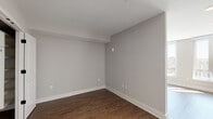 This single-floor space showcases a thoughtfully designed layout that balances open living areas with functional private spaces. The main living area is a standout, featuring large floor-to-ceiling windows that flood the room with natural light while offering expansive city views. Warm-toned hardwood flooring flows throughout, complementing the neutral gray walls and crisp white baseboards, creating a clean and modern aesthetic.

The kitchen is a visual highlight, defined by striking blue cabinetry paired with matte black hardware and a white tile backsplash. Light countertops provide ample workspace, and the kitchen is fully equipped with stainless steel appliances, including a range, built-in microwave, dishwasher, and refrigerator, along with a sleek black-finish sink fixture.

The bedroom offers a quiet, neutral retreat with the same rich hardwood flooring and soft gray walls, providing a calm and versatile canvas. Natural light enters through a nearby window, keeping the space bright and airy.

The bathroom maintains a clean, minimalist design with a soaking tub and shower combination featuring white subway-style tile surround, a light wood vanity with integrated sink, and speckled tile flooring, all finished with brushed nickel fixtures for a polished look.