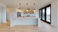 This thoughtfully designed single-floor residence seamlessly blends contemporary style with functional living. The open-concept kitchen is a standout feature, centered around a generous marble-topped island with a gold faucet and undermount sink, illuminated by a row of globe pendant lights. White cabinetry with brass hardware, open wood shelving, white subway tile backsplash, a professional-grade gas range, stainless steel refrigerator, and a wall-mounted range hood complete the culinary space. Light hardwood flooring flows throughout the entire residence, lending warmth and continuity.

The spacious living area is bright and airy, featuring black-framed windows and sliding glass doors that open to a private balcony with urban rooftop views. A built-in shelving unit flanks a brick fireplace, adding character to the room, while a ceiling fan provides comfort year-round.

The bedrooms are clean and well-proportioned, each with light hardwood floors, ceiling fans, and black-framed doors and windows. Select bedrooms offer direct balcony access. The bathrooms are elegantly appointed with marble-topped white vanities, black matte fixtures with gold hardware accents, rounded black-framed mirrors, and hexagonal tile flooring. One bathroom features a striking black grid-framed tub and shower enclosure.