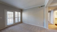 This single-floor residential unit offers a well-organized layout that balances comfort and functionality throughout. The living area is finished with soft neutral-toned carpet and features elegant crown molding along the ceiling, lending a polished, cohesive look. A set of French doors with sidelights opens to a private balcony, allowing natural light to fill the space and providing pleasant outdoor views. An HVAC vent integrated into the ceiling ensures year-round climate comfort.

The bedroom is a generously sized, carpeted retreat with its own window overlooking greenery outside. A ceiling fan with a built-in light fixture adds both practical ventilation and ambient lighting to the room.

The kitchen is equipped with white cabinetry trimmed in warm wood tones, a full suite of white appliances including a refrigerator and electric range, and a sink set into a countertop along one wall. Rich hardwood-style flooring runs throughout the kitchen, adding warmth and contrast to the lighter cabinetry.

The bathroom continues the hardwood-style flooring and features an extended vanity with ample counter space and storage below, a large mirror above, and a separate toilet area. The entry foyer transitions from tile flooring into the carpeted living space, marking a clear and practical boundary at the front door.