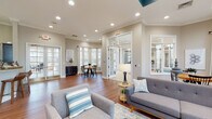 Located at 5710 Arringdon Park Dr in Durham, NC, this single-floor community space offers a thoughtfully designed layout with multiple functional areas connected by rich hardwood flooring and a cohesive neutral color palette. Crown molding and recessed lighting are consistent throughout, lending a polished, professional character to the entire space.

The main lounge area serves as the heart of the space, featuring comfortable mid-century modern seating, generous natural light from large windows dressed with white curtains and blinds, and direct access to adjacent rooms through French-style glass doors. A dedicated dining nook with a round wood table and bay windows offers a bright, welcoming spot for gatherings.

A kitchenette area includes a bar-height counter with wood stools set beneath a decorative arch, complemented by dark cabinetry and direct access to an outdoor patio through glass-paned doors. A secondary lounge room provides a more intimate setting, furnished with cream leather armchairs arranged around small tables, accented by a teal feature wall, ceiling fan, and curated wall art. A smaller, quieter alcove off this room offers a private seating arrangement ideal for one-on-one conversations. Throughout, the space balances openness with defined zones, creating an environment that is both functional and inviting.