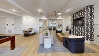 Located at 425 E Foster Crossing Rd in Anna, TX, this single-floor community space offers a thoughtfully designed open-concept layout combining a fully equipped kitchen and a generously sized living area. The interior showcases a modern aesthetic defined by crisp white walls, light wood-look tile flooring, and striking black-and-white graphic wallcoverings that serve as bold focal points throughout.

The living room area is anchored by a statement accent wall featuring a bold brushstroke pattern, a wall-mounted television, and an arrangement of sophisticated seating including neutral sofas and deep navy accent chairs. A sculptural multi-arm pendant light adds an artistic touch overhead, while glass partition walls and French doors allow natural light to flow freely and provide views to adjacent spaces.

The galley-style kitchen is well-appointed with sleek gray cabinetry, white quartz countertops, stainless steel appliances including a full-size refrigerator, a sink, microwave, and dishwasher. Globe pendant lights suspended from chains add warmth and character. A high-top bistro table with woven leather chairs, set beneath the same bold graphic wallcovering, provides a casual seating nook. A dining table with ample seating and a billiards table round out the open entertaining area, making this space as functional as it is visually dynamic.