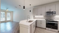 Located at 400 W. Main St in Lewisville, TX, this thoughtfully designed one-bedroom, one-bathroom residence offers a clean, modern aesthetic throughout its single floor. The open-concept layout seamlessly connects the living room, dining area, and kitchen, creating a bright and airy atmosphere. Light wood-look flooring runs throughout the main areas, complementing the neutral color palette.

The contemporary kitchen is a standout feature, equipped with grey shaker-style cabinetry, white quartz countertops, a subway tile backsplash with under-cabinet lighting, and stainless steel appliances including a French door refrigerator, range, and microwave. A kitchen island with a deep single-basin sink and stylish pendant lighting above adds both function and visual appeal.

The living room is filled with natural light from large French doors that open to a private balcony, with a ceiling fan overhead enhancing comfort. The bedroom features plush carpet flooring and a window for additional natural light, with direct access to the full bathroom. The bathroom includes a grey vanity with quartz countertop, a large framed mirror, and an adjacent walk-in closet with built-in shelving. A dedicated laundry area with cabinetry and a pantry complete this well-appointed residence.