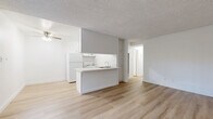 Located at 2700 Ellendale Pl in Los Angeles, CA, this two-bedroom, one-bathroom unit offers a clean, functional layout finished with light wood flooring throughout. The open living area is bright and airy, anchored by a large window with vertical blinds that allow ample natural light, and a ceiling fan overhead. The kitchen features a peninsula with counter seating, white cabinetry with modern brushed nickel hardware, a stainless steel sink, white appliances including a refrigerator and range, and generous upper and lower cabinet storage. The layout flows efficiently from the living area through a connecting hallway to the private quarters. The primary bedroom is generously sized and includes a built-in closet with bifold doors, while the secondary bedroom also offers closet storage and a window for natural light. Both bedrooms share the same consistent wood flooring and neutral white walls found throughout the unit. The full bathroom includes a tiled tub/shower combination, toilet, and vanity. Textured ceilings are present throughout. The overall aesthetic is clean and minimal, offering a neutral, move-in ready canvas in a convenient Los Angeles location.