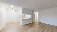 Located at 2700 Ellendale Pl in Los Angeles, CA, this two-bedroom, one-bathroom unit offers a clean, functional layout finished with light wood flooring throughout. The open living area is bright and airy, anchored by a large window with vertical blinds that allow ample natural light, and a ceiling fan overhead. The kitchen features a peninsula with counter seating, white cabinetry with modern brushed nickel hardware, a stainless steel sink, white appliances including a refrigerator and range, and generous upper and lower cabinet storage. The layout flows efficiently from the living area through a connecting hallway to the private quarters. The primary bedroom is generously sized and includes a built-in closet with bifold doors, while the secondary bedroom also offers closet storage and a window for natural light. Both bedrooms share the same consistent wood flooring and neutral white walls found throughout the unit. The full bathroom includes a tiled tub/shower combination, toilet, and vanity. Textured ceilings are present throughout. The overall aesthetic is clean and minimal, offering a neutral, move-in ready canvas in a convenient Los Angeles location.