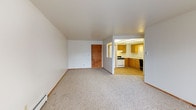 This single-floor residential unit offers a practical and comfortable layout designed for everyday living. The open living area is generously sized, featuring neutral wall-to-wall carpeting, clean white walls, and baseboard heating. A front entry door with an adjacent window allows natural light to flow into the space, creating a bright and welcoming atmosphere.

The kitchen is connected to the living area through an open pass-through layout, showcasing warm honey-toned wood cabinetry, light countertops, a gas range, a dishwasher, and a single-basin sink. A drop ceiling with panel lighting adds a classic touch, while a dedicated pantry closet provides additional storage.

The bedrooms are carpeted and well-proportioned, each offering closet space with wood-trimmed doors. Ceiling fans with integrated light fixtures are present in the bedrooms, contributing to both comfort and functionality. Windows with vertical blinds allow for natural light and outdoor views.

The full bathroom features warm-toned tile flooring, a white tiled tub and shower surround with a curved curtain rod, a toilet, and a wood-trimmed vanity with a sink and mirror. Baseboard heating is also present throughout the unit, ensuring consistent warmth across all rooms.