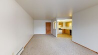 This single-floor residential unit offers a practical and comfortable layout designed for everyday living. The open living area is generously sized, featuring neutral wall-to-wall carpeting, clean white walls, and baseboard heating. A front entry door with an adjacent window allows natural light to flow into the space, creating a bright and welcoming atmosphere.

The kitchen is connected to the living area through an open pass-through layout, showcasing warm honey-toned wood cabinetry, light countertops, a gas range, a dishwasher, and a single-basin sink. A drop ceiling with panel lighting adds a classic touch, while a dedicated pantry closet provides additional storage.

The bedrooms are carpeted and well-proportioned, each offering closet space with wood-trimmed doors. Ceiling fans with integrated light fixtures are present in the bedrooms, contributing to both comfort and functionality. Windows with vertical blinds allow for natural light and outdoor views.

The full bathroom features warm-toned tile flooring, a white tiled tub and shower surround with a curved curtain rod, a toilet, and a wood-trimmed vanity with a sink and mirror. Baseboard heating is also present throughout the unit, ensuring consistent warmth across all rooms.