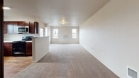 Located at 352 North Beck Road in Post Falls, Idaho, Unit B107 is a single-floor residence that combines practical design with comfortable living spaces. The open-concept layout connects the living area and kitchen, creating a seamless flow throughout the main living space. Plush carpet covers the living area, while wood-look flooring adds warmth in key areas such as the kitchen and bathroom.

The kitchen is well-appointed with rich dark wood cabinetry, light-toned countertops, a stainless steel sink positioned beneath a window with an outdoor view, and stainless steel appliances including a refrigerator and dishwasher. A peninsula counter separates the kitchen from the living area, offering additional workspace and a natural gathering point.

The bedrooms are carpeted and feature neutral walls, generous closet space with built-in shelving and hanging rods, and windows that bring in natural light. The bathroom is finished with warm wood-look flooring, a dark wood vanity with a light stone-style countertop, a large mirror with overhead lighting, and a full soaking tub equipped with a grab bar. Wire shelving provides added storage within the bathroom. Throughout the unit, a neutral color palette and clean lines create a bright, functional, and welcoming atmosphere.