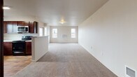 Located at 352 North Beck Road in Post Falls, Idaho, Unit B107 is a single-floor residence that combines practical design with comfortable living spaces. The open-concept layout connects the living area and kitchen, creating a seamless flow throughout the main living space. Plush carpet covers the living area, while wood-look flooring adds warmth in key areas such as the kitchen and bathroom.

The kitchen is well-appointed with rich dark wood cabinetry, light-toned countertops, a stainless steel sink positioned beneath a window with an outdoor view, and stainless steel appliances including a refrigerator and dishwasher. A peninsula counter separates the kitchen from the living area, offering additional workspace and a natural gathering point.

The bedrooms are carpeted and feature neutral walls, generous closet space with built-in shelving and hanging rods, and windows that bring in natural light. The bathroom is finished with warm wood-look flooring, a dark wood vanity with a light stone-style countertop, a large mirror with overhead lighting, and a full soaking tub equipped with a grab bar. Wire shelving provides added storage within the bathroom. Throughout the unit, a neutral color palette and clean lines create a bright, functional, and welcoming atmosphere.