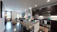 This single-floor residence is designed with a contemporary aesthetic that emphasizes an open, cohesive layout. Polished concrete floors extend throughout, providing a sleek, industrial-modern foundation that contrasts beautifully with the warm, neutral wall tones.

The kitchen is a standout feature, equipped with dark espresso cabinetry reaching toward the ceiling, light granite countertops, a subway tile backsplash, and a full suite of stainless steel appliances including a side-by-side refrigerator, electric range, built-in microwave, and dishwasher. A central island with seating offers additional prep space and a casual dining option, illuminated by elegant globe pendant lights.

The kitchen flows seamlessly into the open living area, which is bright with natural light from multiple windows and features a ceiling fan overhead. The space is generously proportioned and versatile.

Two bedrooms provide comfortable retreats, each with windows admitting natural light. The bathroom connects to one bedroom and includes a dark vanity with granite counters, a large mirror, and a shower with curtain enclosure. The overall ambiance is modern, clean, and thoughtfully designed.