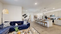 This thoughtfully designed single-floor residence offers 1 bedroom and 2 bathrooms within a well-utilized open-concept floor plan. The kitchen is a standout feature, showcasing granite countertop surfaces, taupe shaker-style cabinetry, a full suite of stainless steel appliances, a white subway tile backsplash, and a generous island with seating for multiple guests — all illuminated by stylish pendant lighting. The kitchen flows seamlessly into the combined dining and living area, which is bathed in natural light from large windows. The living room offers ample space and direct access to an outdoor area via glass doors. Light wood-tone flooring runs consistently throughout the main living spaces, lending a clean, cohesive aesthetic. The primary bedroom is a comfortable retreat with a large window, while the primary bathroom features a double-sink vanity with granite countertops, taupe cabinetry, and a glass-enclosed walk-in shower with tile surround. A dedicated laundry nook with shelving and full hookups adds everyday convenience. A closet provides additional storage. The overall ambiance is bright and modern, with crisp white walls and recessed lighting throughout.