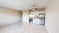 Located at 2497 N Park Ave in Tucson, Arizona, this studio unit offers a practical and efficiently designed single-floor layout. The open main living area is finished with large, light-toned ceramic floor tiles that extend throughout the space, lending a clean and cohesive feel. A ceiling fan with integrated lighting is centrally mounted, providing both air circulation and ambient light. The cinder block walls, painted in a warm neutral tone, reflect the unit's sturdy construction.

The kitchenette is neatly tucked along one wall and features white cabinetry with under-cabinet lighting, a stainless steel refrigerator, a freestanding gas range, and a sink set into a granite-toned countertop. A spacious double-door closet provides ample built-in storage. A window along the exterior wall allows natural light to filter in and offers a view of the surrounding greenery, complemented by a wall-mounted AC unit for climate control.

The bathroom is separately enclosed and includes a full tub/shower combination, a toilet, and a vanity with a sink and mirror — all finished in clean, neutral tones. This unit's straightforward layout and durable finishes make it a functional and easy-to-maintain space in the heart of Tucson.