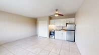 Located at 2497 N Park Ave in Tucson, Arizona, this studio unit offers a practical and efficiently designed single-floor layout. The open main living area is finished with large, light-toned ceramic floor tiles that extend throughout the space, lending a clean and cohesive feel. A ceiling fan with integrated lighting is centrally mounted, providing both air circulation and ambient light. The cinder block walls, painted in a warm neutral tone, reflect the unit's sturdy construction.

The kitchenette is neatly tucked along one wall and features white cabinetry with under-cabinet lighting, a stainless steel refrigerator, a freestanding gas range, and a sink set into a granite-toned countertop. A spacious double-door closet provides ample built-in storage. A window along the exterior wall allows natural light to filter in and offers a view of the surrounding greenery, complemented by a wall-mounted AC unit for climate control.

The bathroom is separately enclosed and includes a full tub/shower combination, a toilet, and a vanity with a sink and mirror — all finished in clean, neutral tones. This unit's straightforward layout and durable finishes make it a functional and easy-to-maintain space in the heart of Tucson.