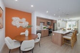 Located at 3585 Aero Ct in San Diego, CA, this thoughtfully designed 2-bedroom, 2-bathroom residence offers a contemporary living experience across a single floor. The open-concept layout seamlessly connects the dining room, kitchen, and living room, creating a bright and airy communal space bathed in natural light from large windows. The kitchen is outfitted with warm wood cabinetry accented by gold hardware, a white quartz countertop island with bar seating, stainless steel appliances, and a classic tile backsplash — all flowing effortlessly into the living area with a ceiling fan overhead. The dining area features a bold terracotta accent wall that adds a warm, modern touch to the entry. The spacious primary bedroom includes a generous walk-in closet with built-in shelving. Both bathrooms are finished with wood-toned vanities, quartz countertops, backlit mirrors, and gold hardware details, with one bathroom featuring a full soaking tub. Additional highlights include five closets, an in-unit laundry area, light wood-toned flooring throughout, and a private balcony overlooking a landscaped courtyard. The building's shared outdoor amenity space is visible from the balcony, offering a lush, well-appointed communal area.