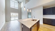 This contemporary two-story residence makes a striking first impression with its dramatic double-height ceilings in the main living area, where expansive floor-to-ceiling windows and a sliding glass door flood the space with natural light and open onto a private balcony with open views of the surrounding cityscape. Light wood-look flooring runs throughout the main level, complementing the bright, neutral palette and modern aesthetic.

The open-concept kitchen is a standout feature, anchored by a large central island with a white quartz countertop and an undermount stainless steel sink, illuminated by a trio of elegant pendant lights. Dark navy cabinetry with sleek hardware provides generous storage, while a full suite of stainless steel appliances — including a refrigerator, range, and microwave — complete the chef-ready setup. A tile backsplash and warm wood flooring add texture and depth.

The upper level offers additional living space, including a carpeted room with an open loft-style overlook enhanced by pendant lighting. The primary bathroom features wood-look tile flooring, dark cabinetry with a white countertop vanity, a soaking tub, and direct access to a walk-in closet with built-in shelving. A second full bathroom includes a tub-shower combo with large-format white tile. A dedicated laundry room houses a full-size washer and dryer with overhead storage shelving, completing this well-appointed home.