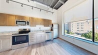 Located at 50 Prince St in Rochester's vibrant East End neighborhood, this one-bedroom, one-bathroom loft delivers an industrial-modern aesthetic throughout. The open-concept main area seamlessly integrates the living, dining, and kitchen spaces beneath dramatically high ceilings with exposed steel beams, ductwork, and track lighting — a hallmark of loft-style design. Light-toned hardwood-style flooring runs throughout, lending warmth and continuity to each room.

The kitchen is well-appointed with warm wood cabinetry, granite-style countertops, and a full suite of stainless steel appliances including a range, microwave, dishwasher, and refrigerator. Large windows in the living area flood the space with natural light and offer open urban views of the surrounding Rochester cityscape.

The bedroom is a comfortable, well-proportioned room with soaring ceilings, large corner windows that frame outdoor views, and ample natural light. Two closets provide generous storage throughout the unit.

The bathroom features a clean, modern design with a walk-in glass-enclosed shower and wood-style flooring. A bright hallway connects the spaces efficiently. The entry features a solid door with modern hardware, opening into the light-filled corridor. This loft-style residence offers a distinctive urban living experience in the heart of Rochester.
