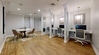 Located at 25 Glenbrook Rd in Stamford, Connecticut, this refined single-floor office space offers a thoughtfully designed professional environment that balances functionality with elegant aesthetics. The space is defined by warm hardwood flooring, crisp white trim, and soft neutral walls accented by decorative crown molding and column details that lend a polished, upscale character throughout.

A striking set of white-framed French doors with glass pane panels serves as a central architectural feature, allowing natural light to flow freely while visually connecting the interior areas. Recessed lighting throughout ensures a bright, well-lit atmosphere suited to productive work.

The layout is efficiently organized, with dedicated workstations separated by white column partitions, each outfitted with a desk, monitor, and ergonomic seating — providing a sense of semi-private focus areas within an open plan. A casual lounge section features a round marble-top table and upholstered seating, offering a welcoming space for meetings or informal collaboration.

Additional details include wall-mounted decorative artwork, built-in HVAC vents, and a private door leading to an adjoining area. The overall ambiance is clean, modern, and professional, making this Stamford office an attractive and highly functional workspace.