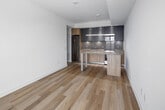 Located at 131 Mill Street in Toronto's vibrant St. Lawrence neighbourhood, this thoughtfully designed one-bedroom, one-bathroom unit offers a clean, modern aesthetic throughout. Light hardwood flooring flows seamlessly across the open-concept layout, enhancing the sense of space and continuity.

The combined kitchen and living area is a standout feature, showcasing a contemporary kitchen outfitted with matte grey upper cabinetry, warm wood-toned lower cabinets, light quartz countertops, stainless steel appliances including a built-in microwave and range, and a central island with a pendant light overhead — ideal for both meal preparation and casual dining.

The bedroom is bright and airy, featuring floor-to-ceiling sliding windows that frame expansive views of the Toronto skyline and surrounding cityscape, flooding the room with natural light. A dedicated closet with built-in shelving and hanging rod provides practical storage.

The bathroom is finished with large-format tile flooring, a soaker tub with a handheld showerhead, a wood-accented vanity, and clean white fixtures. A conveniently positioned in-unit laundry closet houses a stacked Electrolux washer and dryer. The overall design is minimal, functional, and polished, making this an efficient urban retreat.