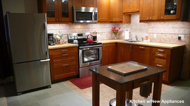 Open concept kitchen with granite-top mobile island and stainless steel refrigerator, range, microwave hood and dishwasher (hidden behind cabinetry) - 2646 Shadow Ln