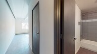 Located at 1525 Yates St in Denver's West Colfax neighborhood, this single-floor unit offers a thoughtfully designed layout with a clean, modern aesthetic. The main living area is bright and open, highlighted by exposed beam ceilings that add architectural character and large windows that invite an abundance of natural light, casting warm patterns across the wood-look tile flooring throughout.

The kitchen is well-appointed with dark cabinetry, wood-grain laminate countertops, and a classic white subway tile backsplash accented by a decorative mosaic tile border — a combination that creates a stylish and functional cooking space. A stainless steel sink and electric range complete the setup.

The bathroom is finished with large-format floor tiles, full-height gray wall tile surrounding the soaking tub and shower combination, and a sleek dark vanity with an integrated white basin, offering a contemporary and cohesive design.

Transitional spaces feature modern dark-framed interior doors that complement the overall color palette, while light-toned tile flooring in the hallway ties the rooms together seamlessly. The unit benefits from multiple windows that ensure consistent natural light throughout, contributing to an airy and welcoming ambiance well-suited to Denver living.