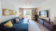 Located at 130 Bowden St in Lowell, MA, this thoughtfully designed single-floor unit showcases a cohesive mid-century modern aesthetic carried throughout every room. The open-concept kitchen features white cabinetry, dark granite countertops, a breakfast bar, and a full suite of stainless steel appliances, including a refrigerator, electric range, and over-the-range microwave. Adjacent to the kitchen, a dedicated dining area provides a comfortable space for meals. The living room is bright and welcoming, anchored by light hardwood flooring, a large sliding glass door that opens to a private outdoor patio with garden views, and a well-curated entertainment setup with a wall-mounted TV and a warm mix of seating. The primary bedroom is a standout space, featuring bold golden-yellow geometric wallpaper, recessed lighting, soft carpet flooring, and a mid-century wood desk with a round mirror. The second bedroom is painted in a soothing aqua tone, filled with natural light from a large window, and accented with gold fixtures and plush carpet. The bathroom is clean and functional, with a full tub-shower combination, white cabinetry with built-in shelving, and wood-look flooring. Throughout the unit, a vibrant yellow, navy, and teal color palette ties the design together with personality and warmth.