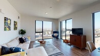 Located at 1225–1243 5th St in Oakland, CA, this modern single-floor residence is designed with a clean, contemporary aesthetic throughout. The living area is a standout feature, defined by expansive floor-to-ceiling windows on two sides that frame sweeping views of the Oakland cityscape, surrounding infrastructure, and the bay beyond. Natural light fills the space generously, highlighting the warm wood-style flooring that runs throughout the main living areas. The open layout connects the living room seamlessly to the kitchen, which is outfitted with stainless steel appliances—including a gas range, microwave, and dishwasher—paired with light wood cabinetry, white quartz countertops, and a undermount sink. The unit includes two bedrooms, each with built-in closets and neutral carpeting. The primary bedroom benefits from an en-suite bathroom featuring a white vanity with quartz countertops, while a second full bathroom includes a tub-shower combination with clean tile surround. Throughout the unit, the design maintains a bright, minimalist palette with white walls and modern fixtures, creating a cohesive and functional living environment.