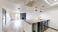Located at 7302 University Row in San Antonio, TX, this two-story, 2-bedroom, 2-bathroom home is thoughtfully designed across two well-proportioned floors. The main level features an open-concept kitchen and living area finished with light wood-look flooring. The kitchen is a standout, boasting a granite countertop island with an undermount sink and gold-tone faucet, dark cabinetry with gold hardware, a white subway tile backsplash, stainless steel refrigerator, and black appliances. Industrial-style pendant lights illuminate the island, while a skylight adds natural brightness. The living room is anchored by a dramatic floor-to-ceiling black brick fireplace and a sliding glass door that opens to the outdoors, filling the space with natural light. A staircase leads to the upper level, where both carpeted bedrooms offer quiet retreats. The spacious primary bedroom includes natural light from a window and ample closet space. Both bathrooms feature dark cabinetry with gold accents and marble-style countertops, with one including a tub-shower combo. Textured ceilings are present throughout, contributing to the home's classic character.