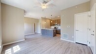 This 2-bedroom, 1-bathroom single-floor unit offers a thoughtfully designed open-concept layout that maximizes its compact footprint. Light-toned luxury vinyl plank flooring flows seamlessly throughout the entire space, creating a cohesive and modern aesthetic. The open living and kitchen area serves as the heart of the unit, anchored by a peninsula-style kitchen island with a white countertop and integrated sink. Warm medium-tone wood cabinetry lines the kitchen walls, complemented by a full suite of stainless steel appliances including a refrigerator, range, and microwave. Pendant lighting above the island and a ceiling fan in the living area add functional style. Neutral warm-beige walls provide a clean, versatile backdrop throughout. The primary bedroom features a walk-in closet with wire shelving and benefits from a large window that brings in generous natural light with outdoor views. The secondary bedroom also offers closet access and a similarly bright, open feel. The full bathroom includes a contemporary blue-toned vanity with storage cabinetry, a mirror, and a window for natural ventilation. A dedicated laundry area completes this efficiently planned unit, offering practical convenience within a clean, move-in-ready space.