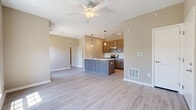 This 2-bedroom, 1-bathroom single-floor unit offers a thoughtfully designed open-concept layout that maximizes its compact footprint. Light-toned luxury vinyl plank flooring flows seamlessly throughout the entire space, creating a cohesive and modern aesthetic. The open living and kitchen area serves as the heart of the unit, anchored by a peninsula-style kitchen island with a white countertop and integrated sink. Warm medium-tone wood cabinetry lines the kitchen walls, complemented by a full suite of stainless steel appliances including a refrigerator, range, and microwave. Pendant lighting above the island and a ceiling fan in the living area add functional style. Neutral warm-beige walls provide a clean, versatile backdrop throughout. The primary bedroom features a walk-in closet with wire shelving and benefits from a large window that brings in generous natural light with outdoor views. The secondary bedroom also offers closet access and a similarly bright, open feel. The full bathroom includes a contemporary blue-toned vanity with storage cabinetry, a mirror, and a window for natural ventilation. A dedicated laundry area completes this efficiently planned unit, offering practical convenience within a clean, move-in-ready space.
