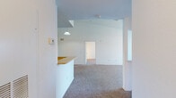 This single-floor residence offers a practical and well-organized layout across several distinct living areas. The main living space immediately impresses with its vaulted ceiling, which lends a sense of openness and volume rarely found in similarly scaled homes. A pendant light fixture adds a focal point overhead, while neutral carpet and crisp white walls create a clean, versatile backdrop. A breakfast bar with a light countertop separates the living area from the kitchen, providing both visual definition and functional convenience.

The kitchen is designed in a galley configuration, featuring warm-toned wood cabinetry, a white electric range, a dishwasher, a refrigerator, and a double sink integrated into a white peninsula. Wood-look vinyl flooring runs throughout the kitchen, adding durability and a grounded aesthetic contrast to the carpeted living areas.

The bedrooms are generously proportioned, each equipped with ceiling fans and plush carpeting. Closet space is well-considered, with at least one room offering a walk-in closet and another featuring a built-in shelving system behind mirrored sliding doors. Natural light enters through windows, enhancing the overall brightness.

The bathrooms include tiled tub-and-shower combinations, warm wood-toned vanity cabinetry, and wood-look vinyl flooring, offering a cohesive and functional finish throughout.