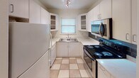 Located in Austin's desirable 78704 neighborhood, this single-story home offers a practical and comfortable layout with consistent design choices throughout. The entryway welcomes visitors through a white paneled door with a fan-light transom window, opening onto warm wood-look flooring that extends through the main living areas and bedrooms, creating a cohesive and inviting atmosphere.

The kitchen is efficiently laid out in a U-shaped configuration, featuring crisp white cabinetry with open display shelving, light countertops with a dark tile backsplash, and a full suite of appliances including a black electric range, stainless steel over-the-range microwave, and a white refrigerator. Light tile flooring and a window above the sink provide natural light to the space.

The living and bedroom areas are bright and airy, each equipped with ceiling fans with integrated lighting and generous wall space. Natural light filters in through windows fitted with blinds. The bathroom includes a full tub-and-shower combination with tile surround, tile flooring, and a frosted window that allows natural light while maintaining privacy. A utility area with an accessible electrical panel adds practical functionality to the home's overall well-organized floor plan.