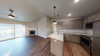 This single-floor home is designed with a modern, open-concept layout that seamlessly connects the kitchen, dining, and living areas. The living room is anchored by a stone-surround fireplace and benefits from vaulted ceilings that amplify the sense of space. Large sliding doors allow natural light to pour across the dark hardwood-style flooring, enhancing the warm, neutral color palette throughout.

The kitchen is well-appointed with taupe cabinetry, light granite countertops, a peninsula with an undermount sink, and stainless steel appliances including a refrigerator, range, and microwave. Stylish pendant lights hang above the peninsula, complementing the recessed lighting overhead.

The bedrooms are carpeted and bright, each featuring windows that bring in natural light. One bedroom includes a ceiling fan and wall-mounted climate control unit with a baseboard heater. Two bathrooms serve the home — one with a soaking tub and one with a walk-in shower — both featuring granite-topped vanities and wood-style flooring. A dedicated laundry area houses a full-size front-loading washer and dryer with overhead shelving, adding everyday convenience to this thoughtfully designed home.